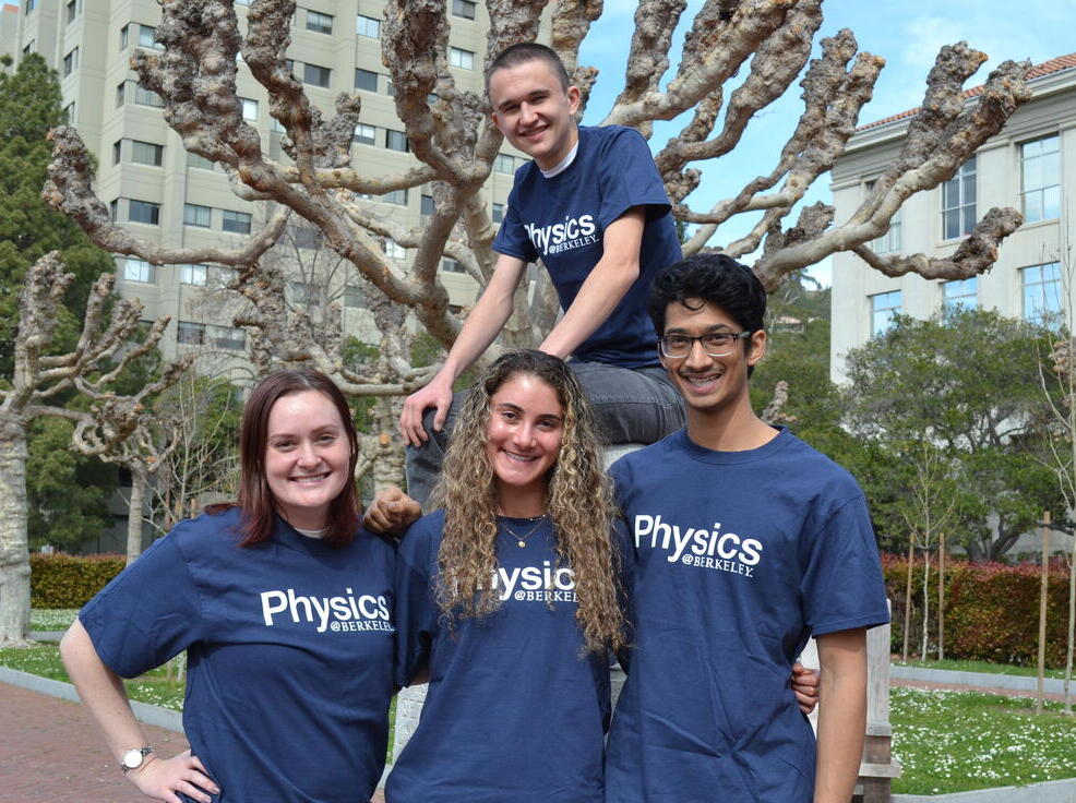 4 students wearing blue Berkeley Physics tee shirts standing in the campanile esplanade