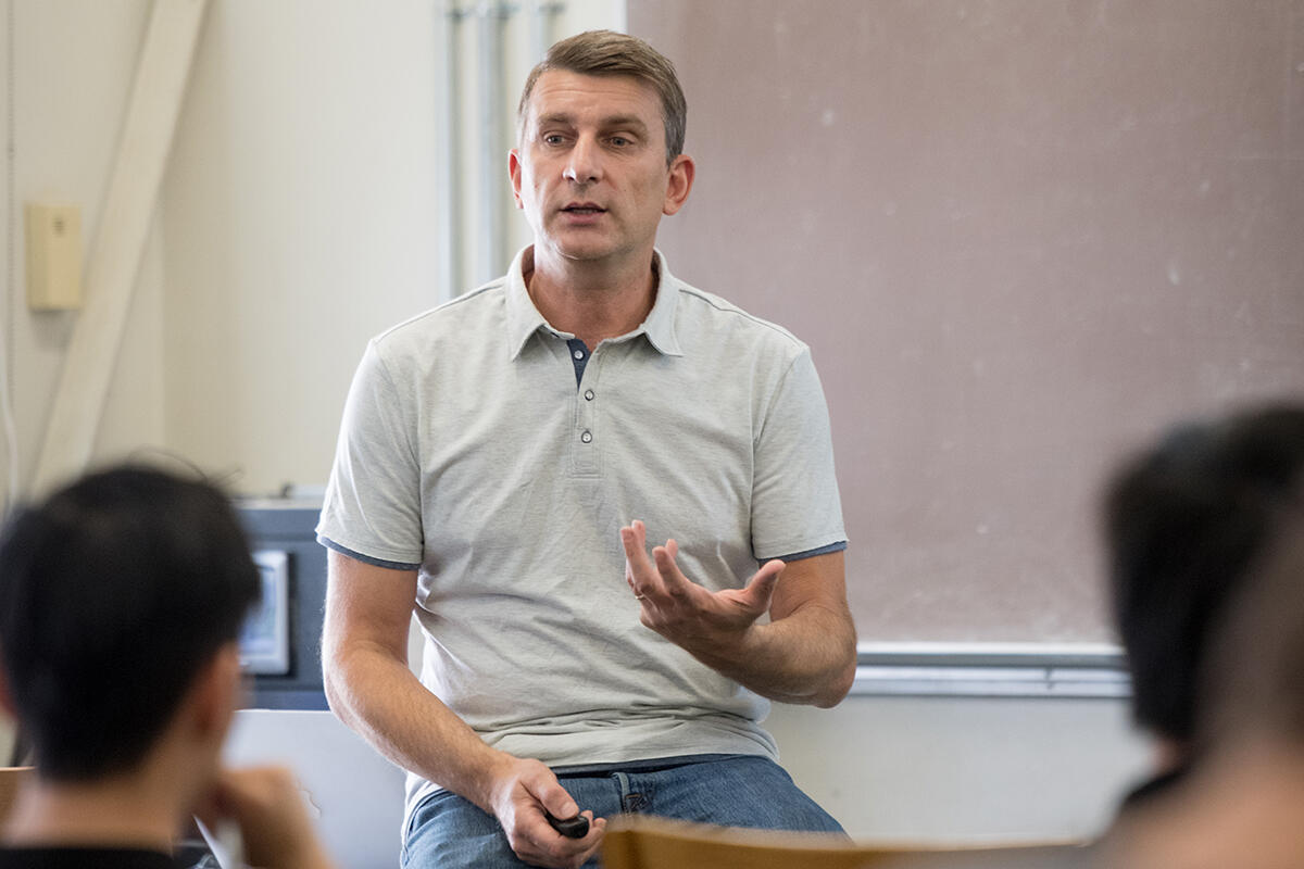 Professor sitting on edge of desk teaching students in classroom