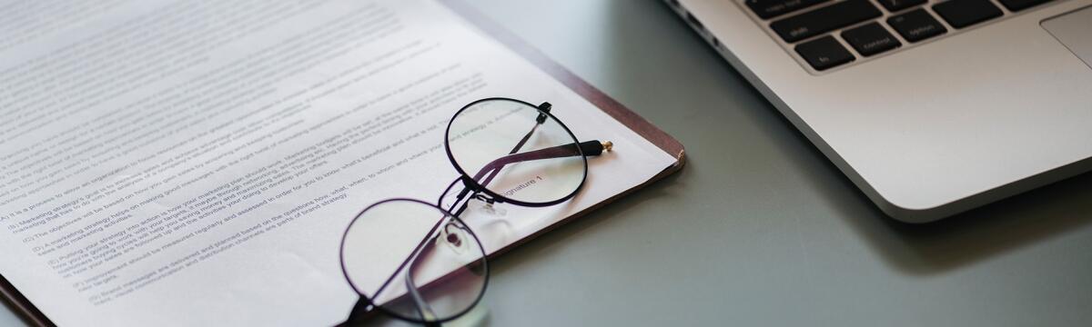 Reimbursements printed document with folded eyeglasses on top, next to a laptop computer