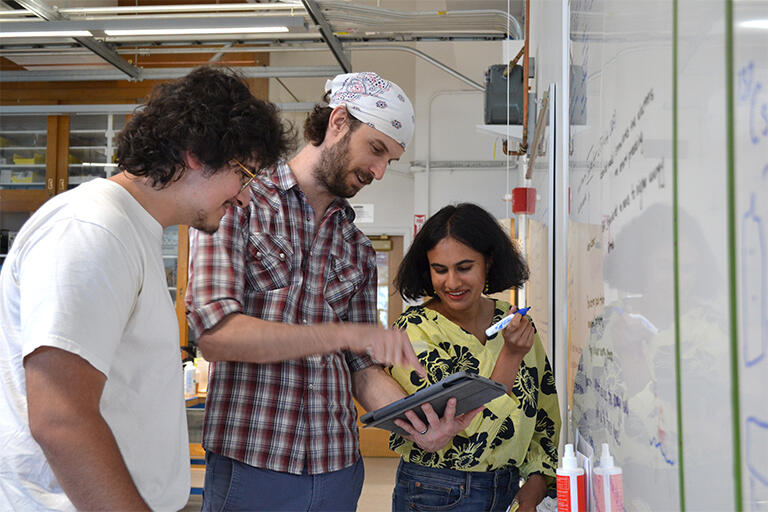 3 students organizing their projects at the white board in the 111 Lab