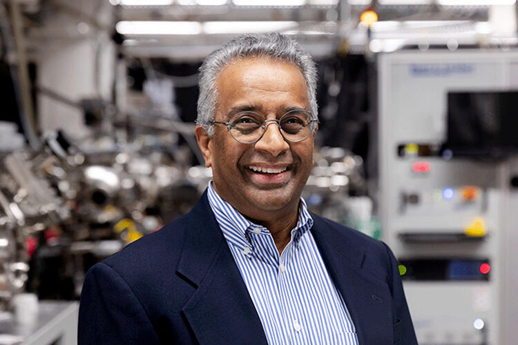 Photo of R. Ramesh smiling in a blue suit and striped shirt, standing in the lab